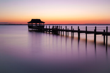 a lonely dock at sunset extends into the sound on the outer banks of north carolina.