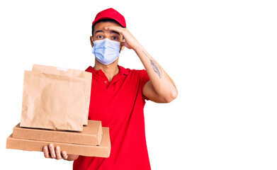 Fototapeta na wymiar Young handsome hispanic man delivering food wearing covid-19 safety mask stressed and frustrated with hand on head, surprised and angry face