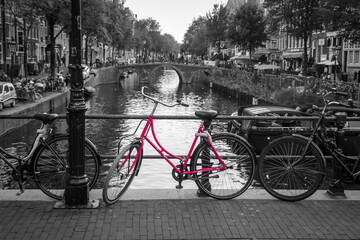 Fototapeta na wymiar A picture of a pink bike on the bridge over the channel in Amsterdam. The background is black and white.