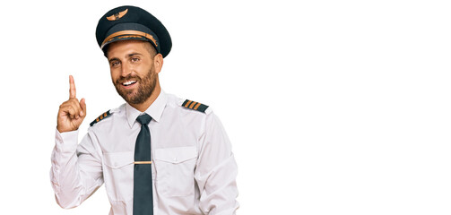 Handsome man with beard wearing airplane pilot uniform showing and pointing up with finger number one while smiling confident and happy.