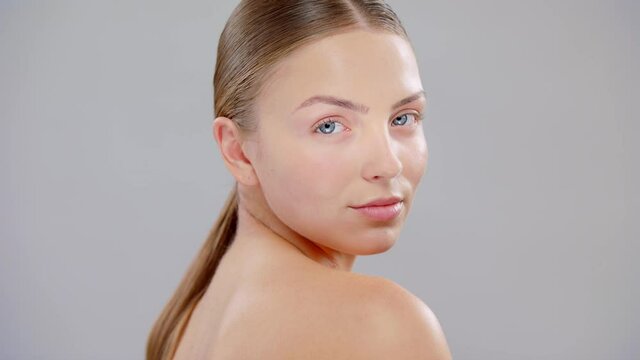 Close Up Beautiful Young Caucasian Blonde Woman With Blue Eyes And Smooth Healthy Skin Looking To The Camera Skin Care Cosmetic Concept. Slow Motion On Grey Background.