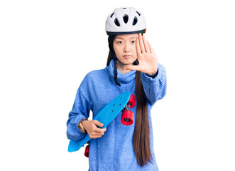Young beautiful chinese woman wearing security helmet holding skate with open hand doing stop sign with serious and confident expression, defense gesture