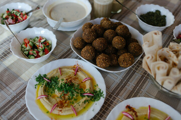 A table spread of middle-eastern dishes like hummus and falafel and salad