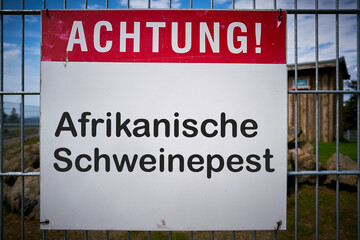 Schild mit der Aufschrift "Achtung Afrikanische Schweinepest" an einem Zaun zu einem Bauernhof 