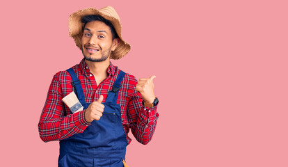 Handsome latin american young man weaing handyman uniform pointing to the back behind with hand and thumbs up, smiling confident