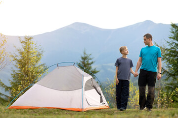 Father with his child son walking together near a tent in summer mountains. Active family recreation concept.