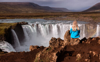 a girl in iceland is looking at godafoss waterfall