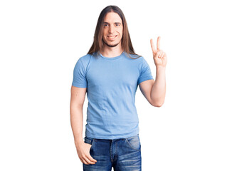 Obraz na płótnie Canvas Young adult man with long hair wearing casual clothes smiling with happy face winking at the camera doing victory sign. number two.