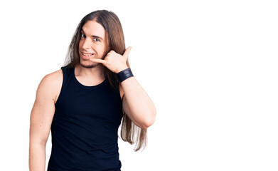 Fototapeta premium Young adult man with long hair wearing goth style with black clothes smiling doing phone gesture with hand and fingers like talking on the telephone. communicating concepts.