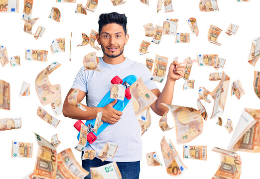 Handsome latin american young man holding skate smiling happy pointing with hand and finger to the side