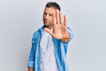 Handsome muscle man wearing casual denim jacket doing stop sing with palm of the hand. warning...