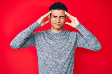 Young handsome hispanic man over red background suffering from headache desperate and stressed because pain and migraine. hands on head.