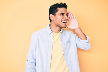 Young handsome hispanic man standing over yellow background shouting and screaming loud to side with hand on mouth. communication concept.