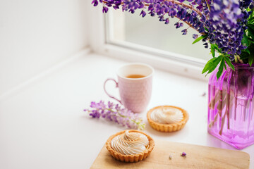 selective focus. still life of green tea in a beautiful mug with cakes tart. nice breakfast. table setting with fresh flowers.