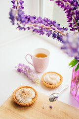 selective focus. still life of green tea in a beautiful mug with cakes tart. nice breakfast. table setting with fresh flowers.