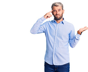 Young handsome blond man wearing elegant shirt confused and annoyed with open palm showing copy space and pointing finger to forehead. think about it.