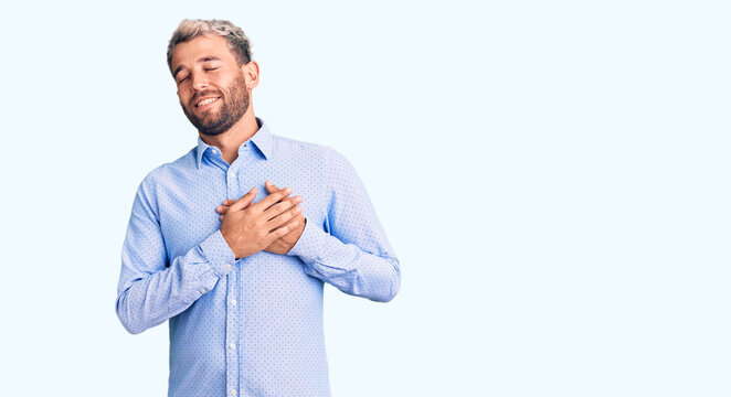 Young handsome blond man wearing elegant shirt smiling with hands on chest with closed eyes and grateful gesture on face. health concept.