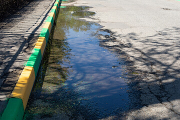 A large puddle along the yellow green border. Poor asphalt paving on a city road. Puddle on the road