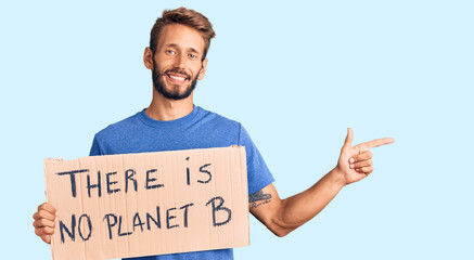 Handsome blond man with beard holding there is no planet b banner smiling happy pointing with hand...