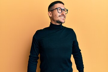 Fototapeta premium Handsome man with tattoos wearing turtleneck sweater and glasses looking away to side with smile on face, natural expression. laughing confident.