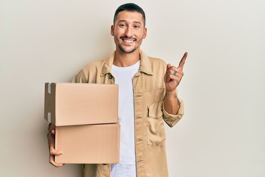 Handsome man with tattoos holding delivery package smiling happy pointing with hand and finger to the side