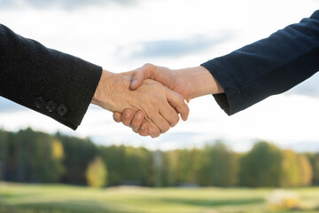 Handshake of two contemporary successful business partners against green trees