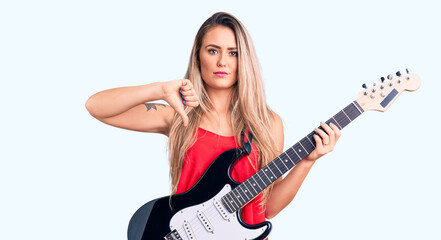 Obraz na płótnie Canvas Young beautiful blonde woman playing electric guitar with angry face, negative sign showing dislike with thumbs down, rejection concept