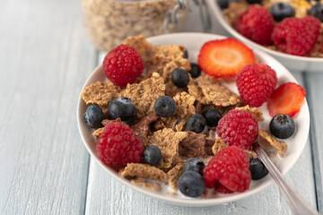 Granola with blueberries and raspberries in white bowl on dark white desk.