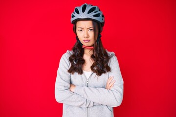 Young beautiful chinese girl wearing bike helmet skeptic and nervous, disapproving expression on face with crossed arms. negative person.