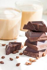 Pieces of dark chocolate, coffee beans and cups of cocoa or coffee with milk on white background. Good morning or happy day concept.