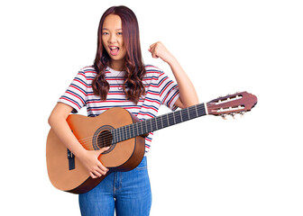 Young beautiful chinese girl playing classical guitar screaming proud, celebrating victory and success very excited with raised arms