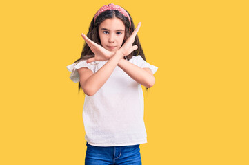 Cute hispanic child girl wearing casual white tshirt rejection expression crossing arms doing negative sign, angry face