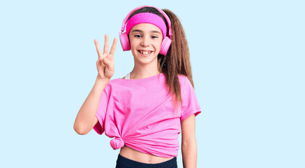 Obraz na płótnie Canvas Cute hispanic child girl wearing gym clothes and using headphones showing and pointing up with fingers number three while smiling confident and happy.