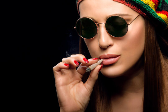 Attractive young woman smoking a marijuana cigarette. Close-up face portrait isolated on black