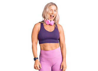 Middle age fit blonde woman wearing gym clothes and using headphones winking looking at the camera...