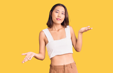 Young beautiful chinese girl wearing casual clothes clueless and confused expression with arms and hands raised. doubt concept.