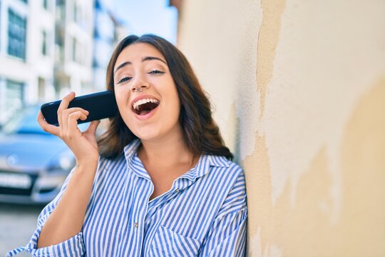 Young hispanic businesswoman smiling happy listening audio message using smartphone at the city.