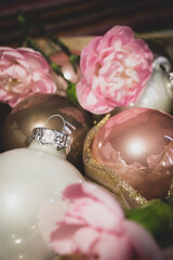 Close-up of Christmas baubles in a wooden tray decorated with golden glitter balls and pink carnations. Matte image