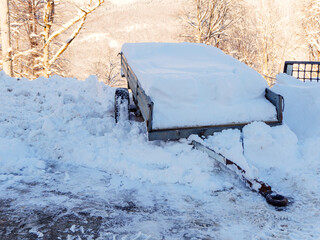 A cart filled with snow stands in a snowdrift against a background of wooded mountains and trees