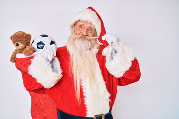 Old senior man with grey hair and long beard wearing santa claus costume holding mustache smiling with a happy and cool smile on face. showing teeth.