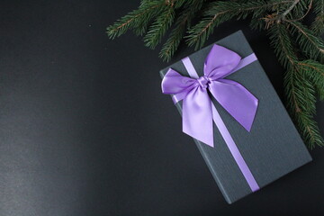 new year's Christmas background a branch of spruce pine trees on a black background and a gift box black gift box with lilac purple fuchsia ribbon and bow minimalism top view from copy space