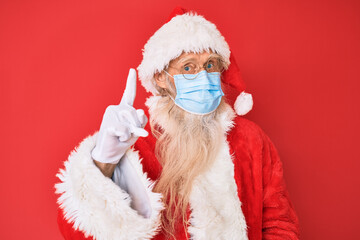 Old senior man wearing santa claus costume wearing safety mask smiling with an idea or question pointing finger up with happy face, number one