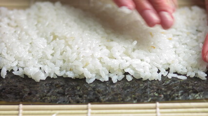 Spreading Cooked Sushi Rice On A Seaweed Wrap - Sushi Making - close up, slow motion.Sushi Chef Spreading Japanese Sushi Rice On Nori Sheet For A Delicious Sushi Rolls high angle shot