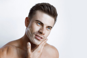 Fototapeta na wymiar Muscular sexy model sports young man on white background. Portrait of beautiful smiling healthy guy applying foam for washing on his face. Facial skincare routine.