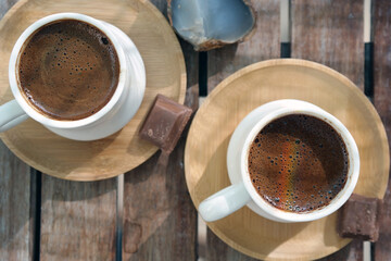 Turkish coffee with foam on top , made of fresh roasted and fine ground coffee beans, served in small ceramic cups on bamboo plates with Turkish delight or bitter chocolate pieces after breakfast