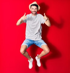 Young handsome hispanic man wearing casual clothes and summer hat smiling happy. Jumping with smile...