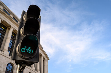 A bicycle traffic light in London, UK.  The traffic light is green to cycle. Old building in the background. Blue sky with white clouds provides copy space. Green light for cycles in London.