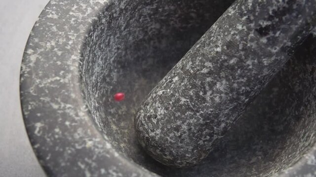 Close-up of rose-red peppercorns falling into the grey stone mortar in slow motion