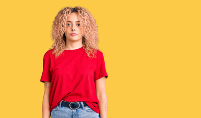 Young blonde woman with curly hair wearing casual red tshirt relaxed with serious expression on face. simple and natural looking at the camera.