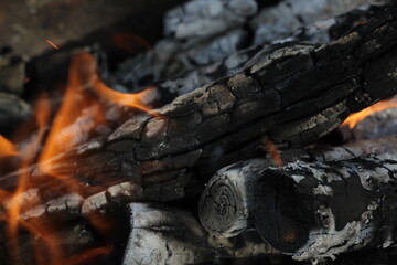 Fototapeta premium Smoldered logs burned in vivid fire close up. Atmospheric background with flame of campfire. Unimaginable detailed image of bonfire from inside with copy space. Whirlwind of smoke and glowing embers.